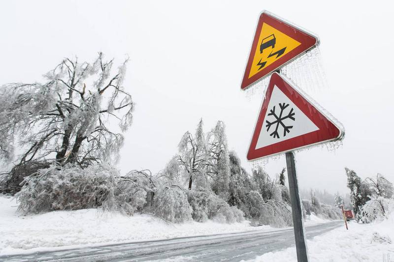 Slippery road and icicle road signs along road covered in snow