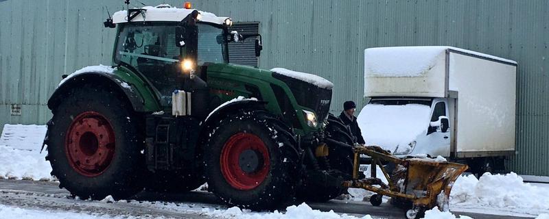 Green tractor with digger on snow-covered road